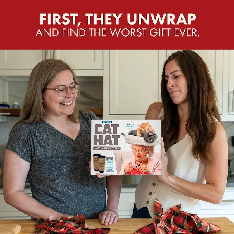 Two women laughing while holding a "Cat Hat" gift box in a kitchen.