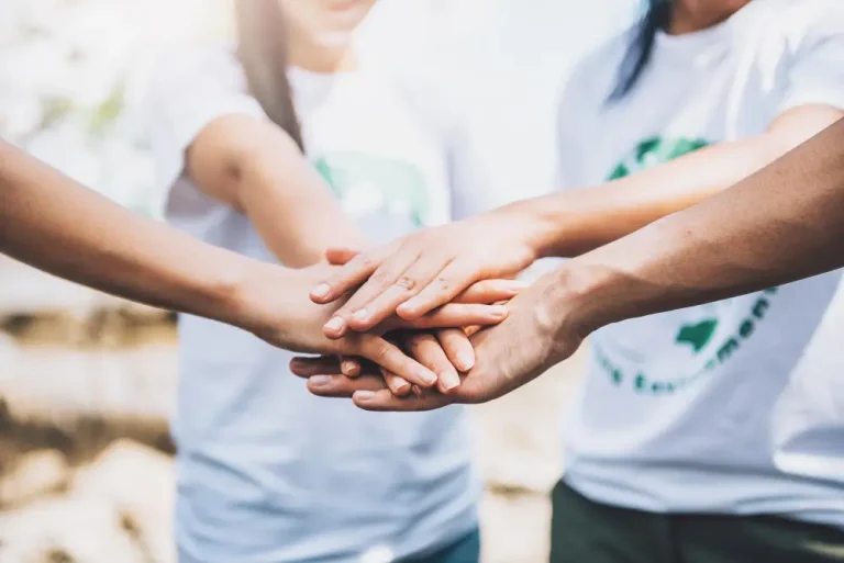Hands of three people wearing white t-shirts joined together in solidarity.